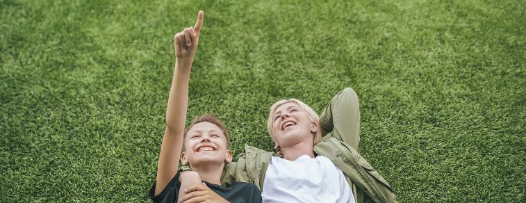 A woman and a boy lay on the grass and pointing out clouds.