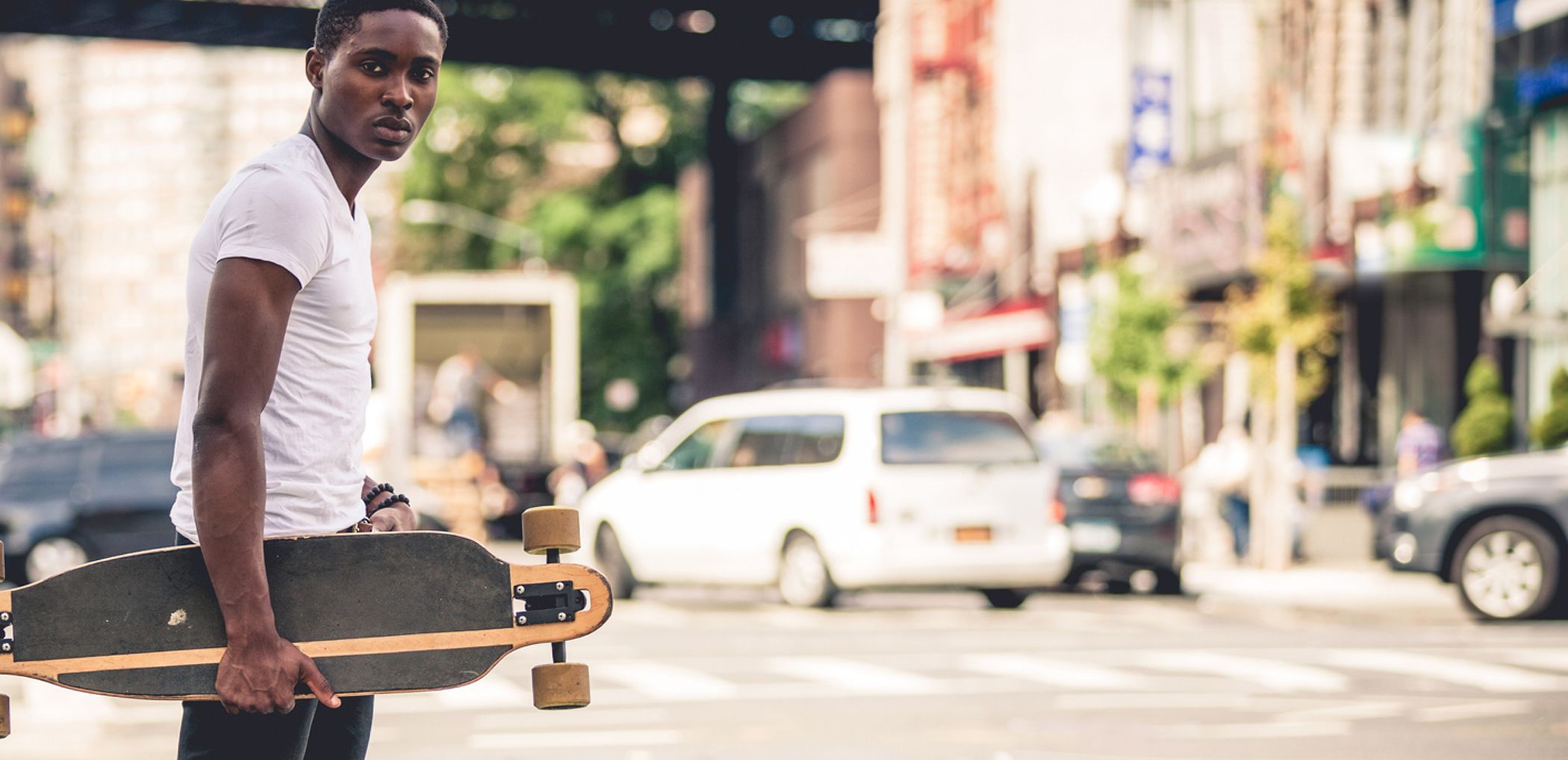 A teenager holds on to a skateboard as he crosses the street.
