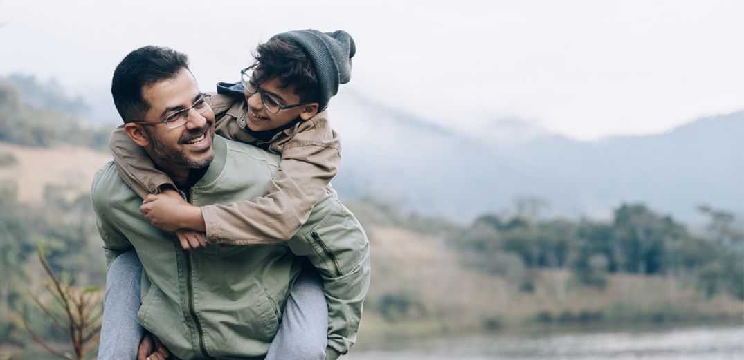 A dad gives his son a piggyback ride on a hike.
