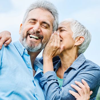 A retiree playfully whispers into her partner's ear as he laughs.