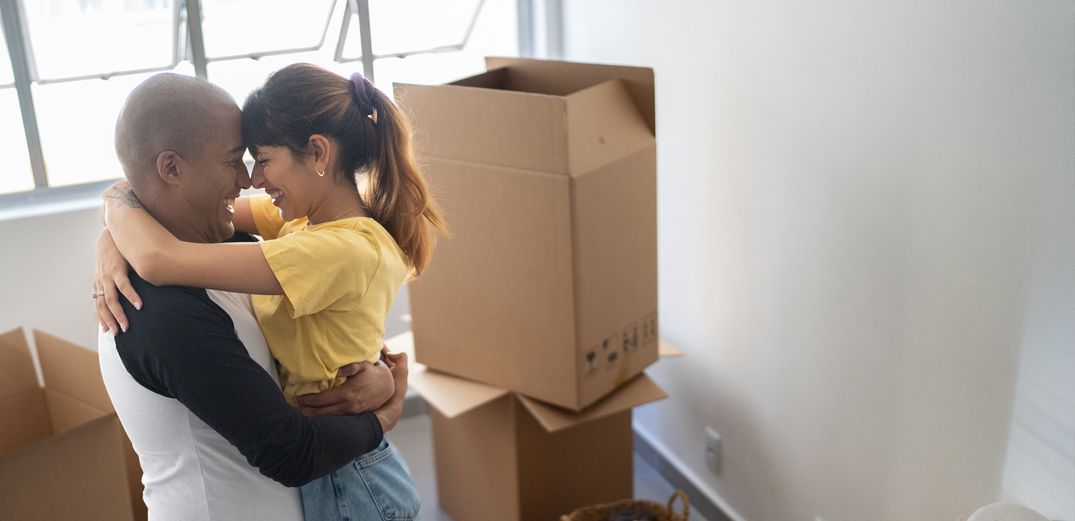 A couple hugs in front of moving boxes in their new home.