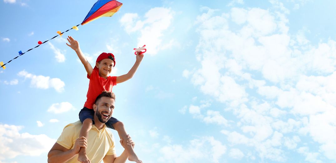 A dad flies a kite with his son sitting on his shoulders.