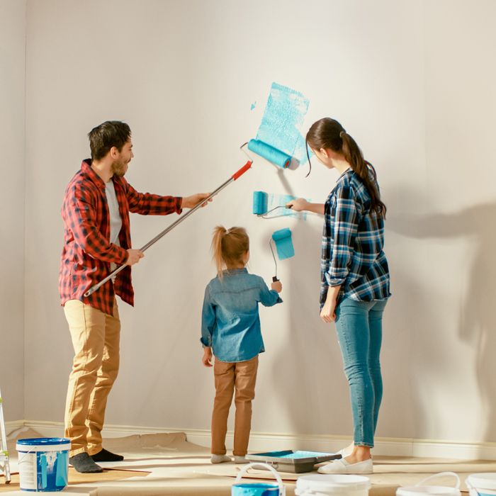 A mom, dad and daughter painting a wall turquoise.