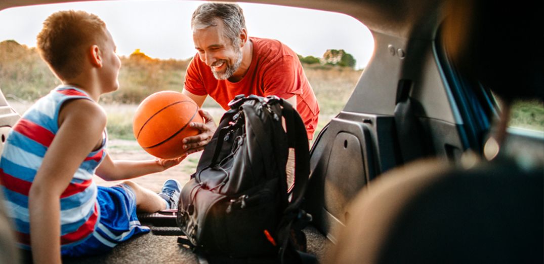 A father and son grab their basketball gear from the back of an SUV.
