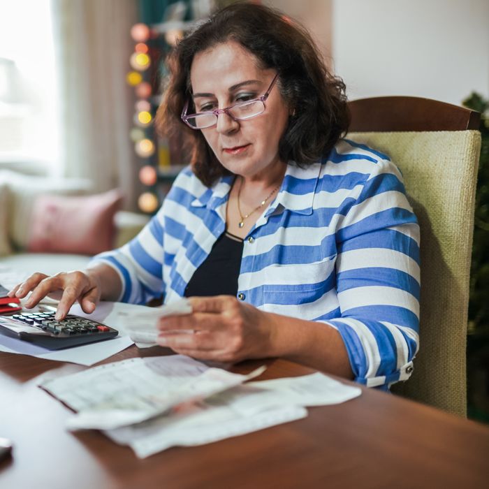 A woman in glasses adds up her receipts at a kitchen table.