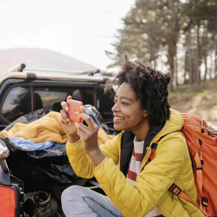 A camper uses her phone to take a picture from the back of a pickup truck filled with camping gear.
