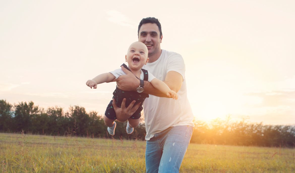 A Patelco member holds up his baby to help him 'fly' outside.