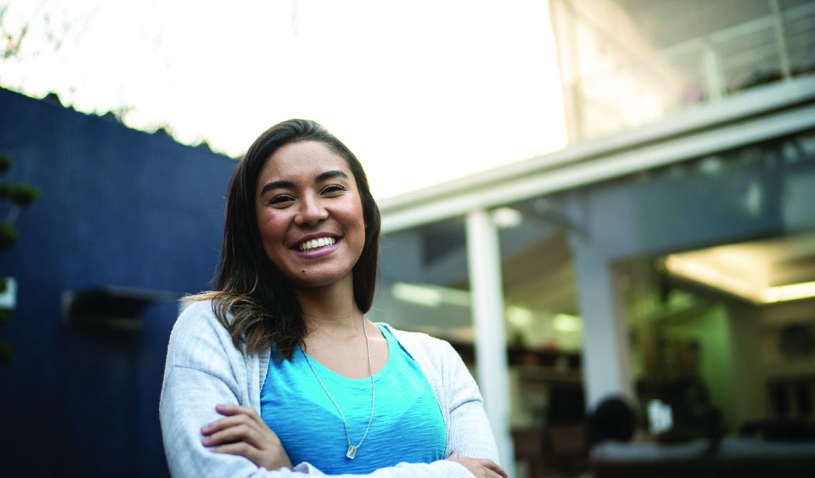 A smiling Patelco member stands in front of a modern home.