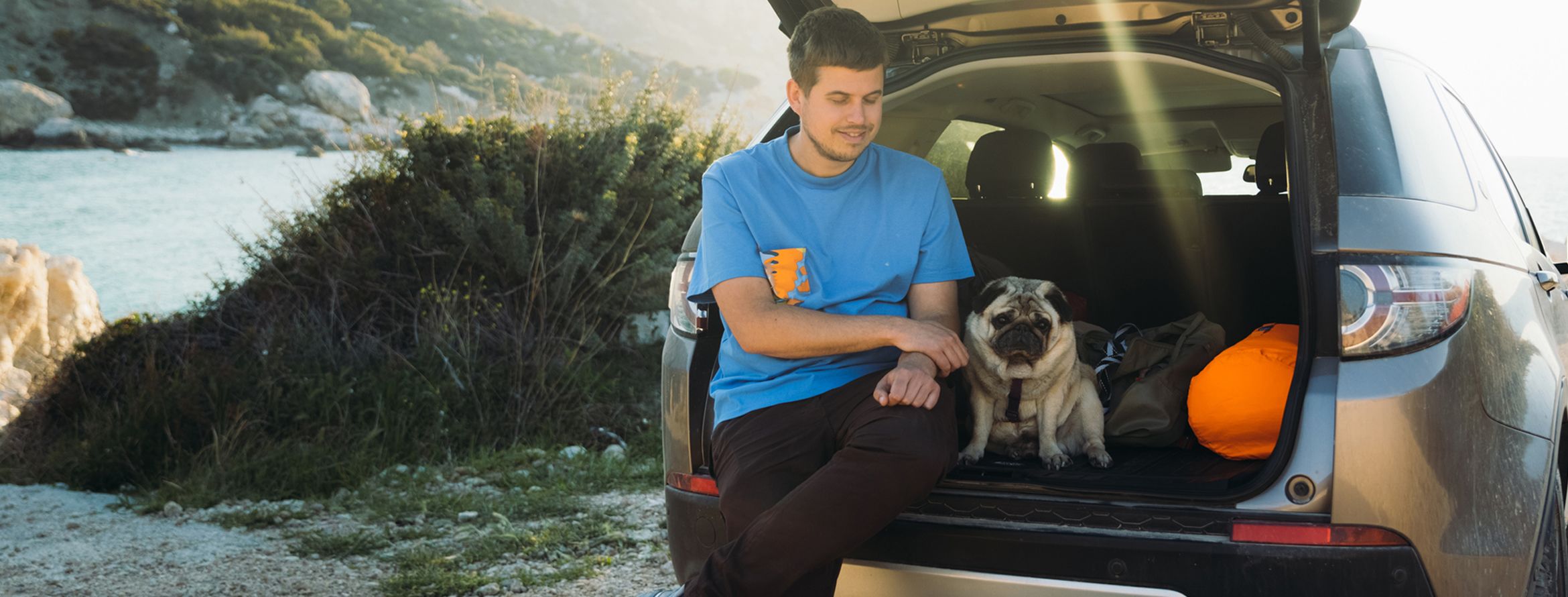 A hiker pets a pug in the back of his new car.