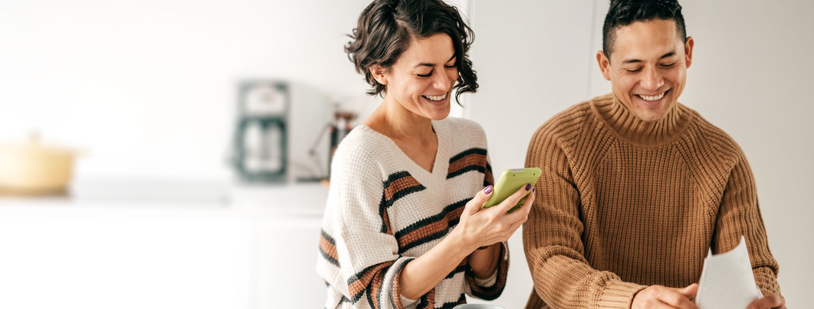 A smiling woman checks her IRA account from Patelco's mobile app as a man sorts papers.