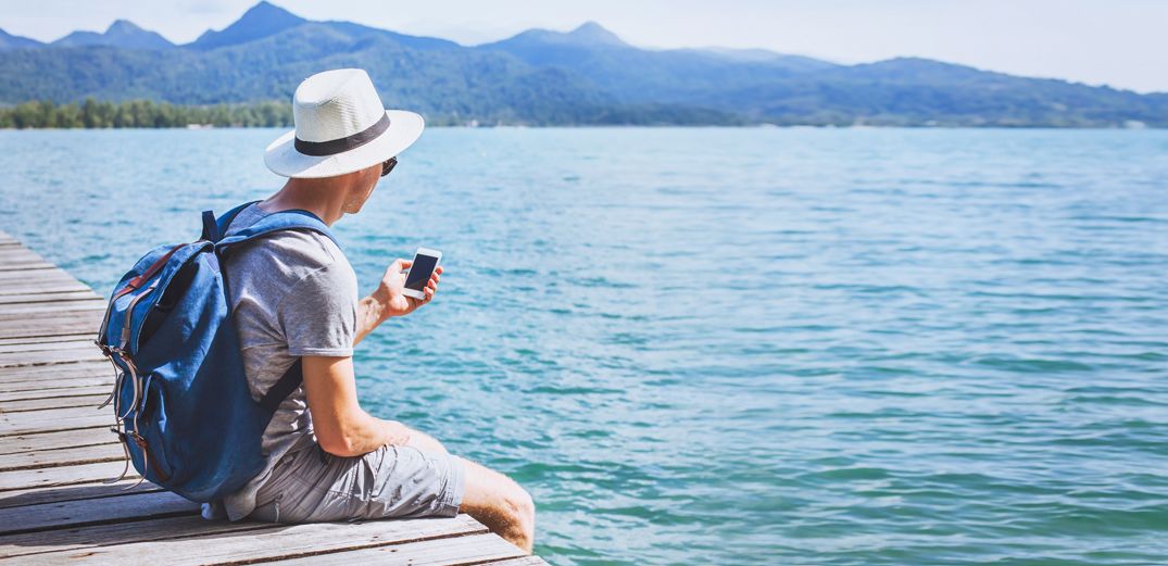 A man checks his Patelco Online account while enjoying a lake view from the edge of a dock.