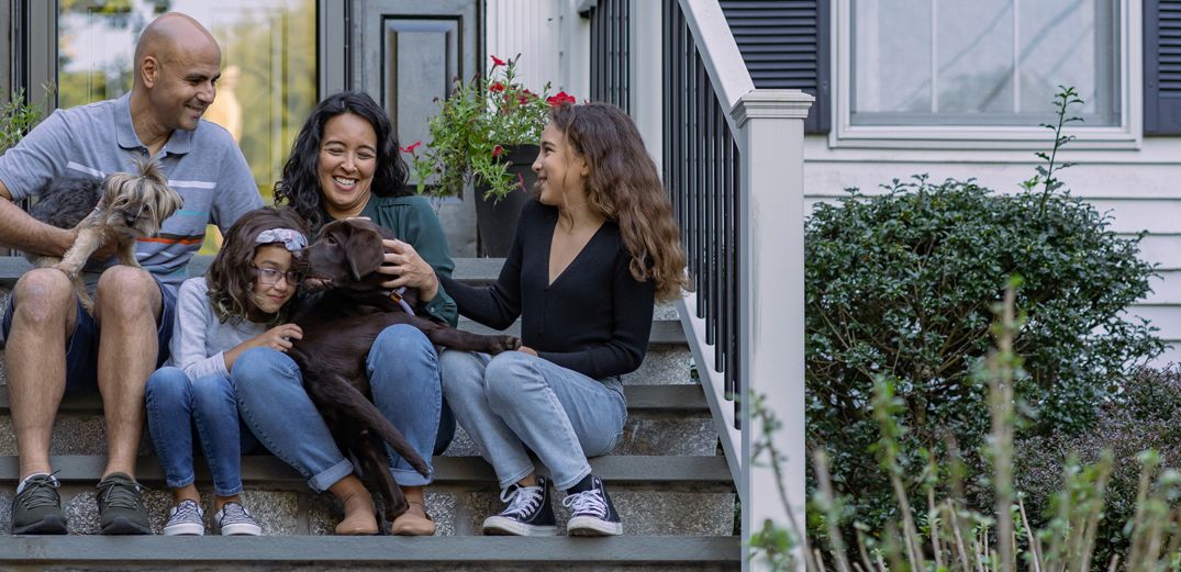 A family of four- plus their two dogs - sit on their front stoop.