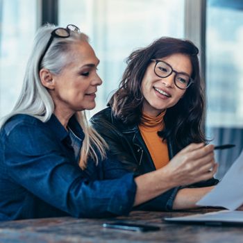 Two smiling women review financial paperwork.