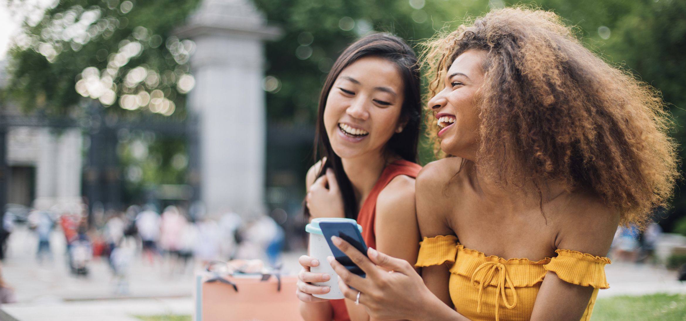 Two teenage friends laughing outside as they look at something on a mobile phone