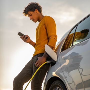 Person on their phone leaned up against their electric vehicle while it charges