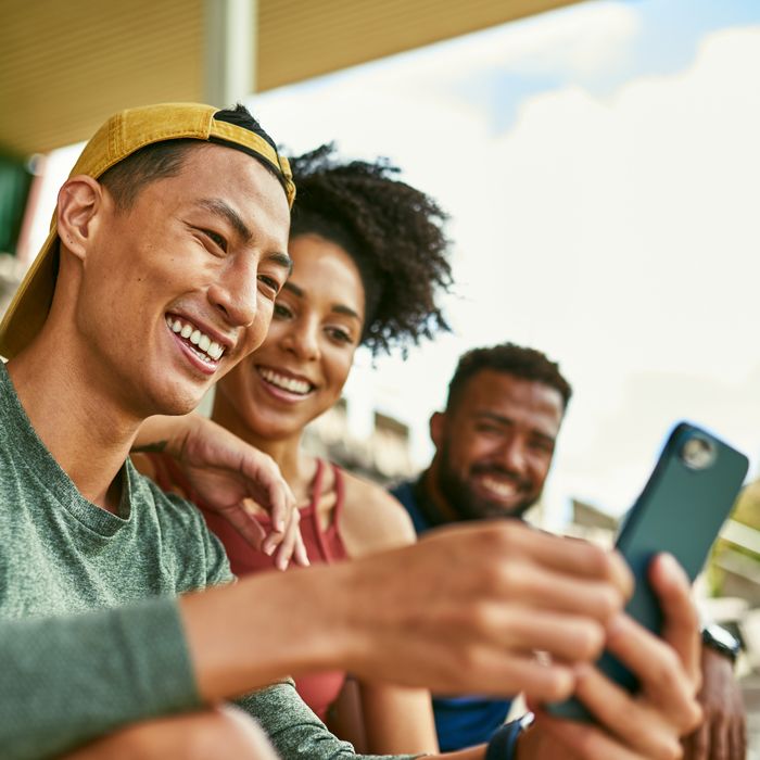 Friends gathered outside looking at something on a mobile device that causes laughter