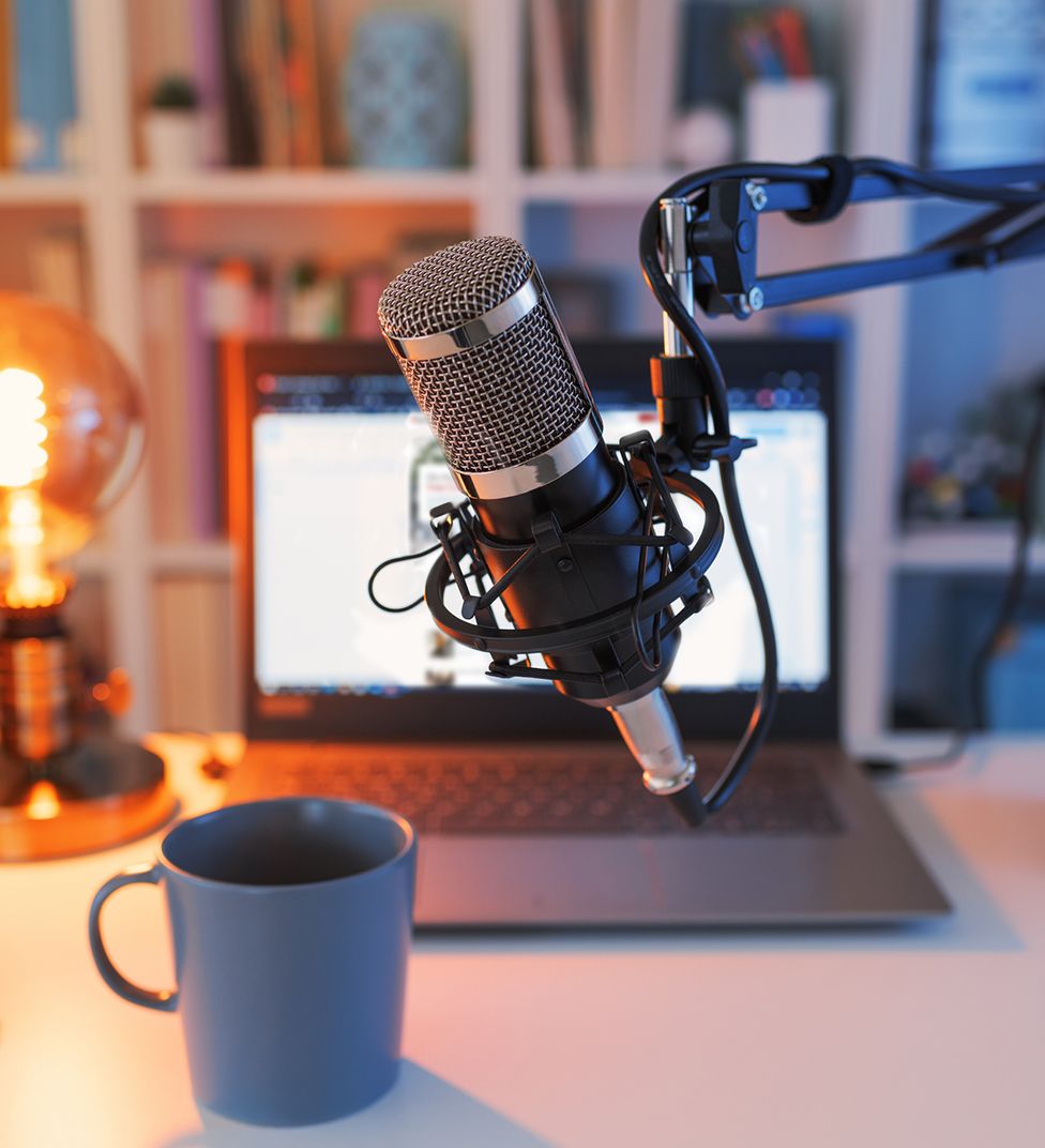 A podcast microphone in front of a laptop and a coffee mug