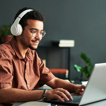 Patelco member wearing headphones at a desk on a laptop perusing fraud tips