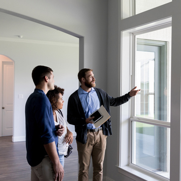 A realtor showing a young couple a window in a house during a tour