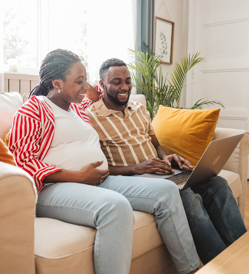 Happy black husband and pregnant wife shopping online at home.